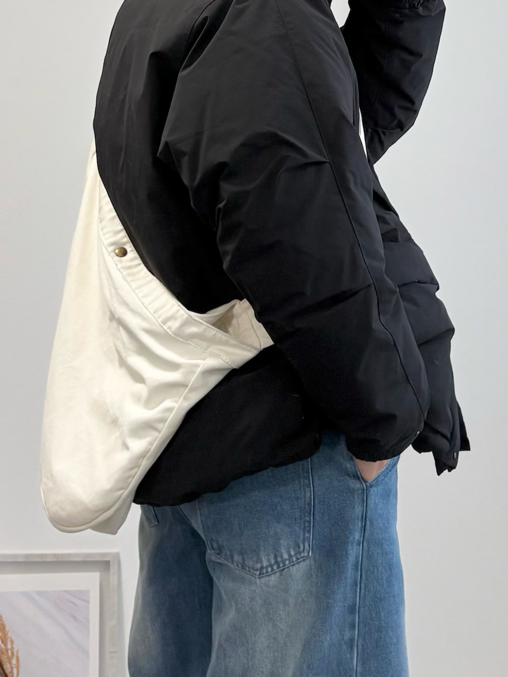 ブラック系のダウンジャケット/コート、ベージュ系のショルダーバッグ、ブルー系のデニムパンツを着用したメンズの冬コーディネートの4枚目の写真