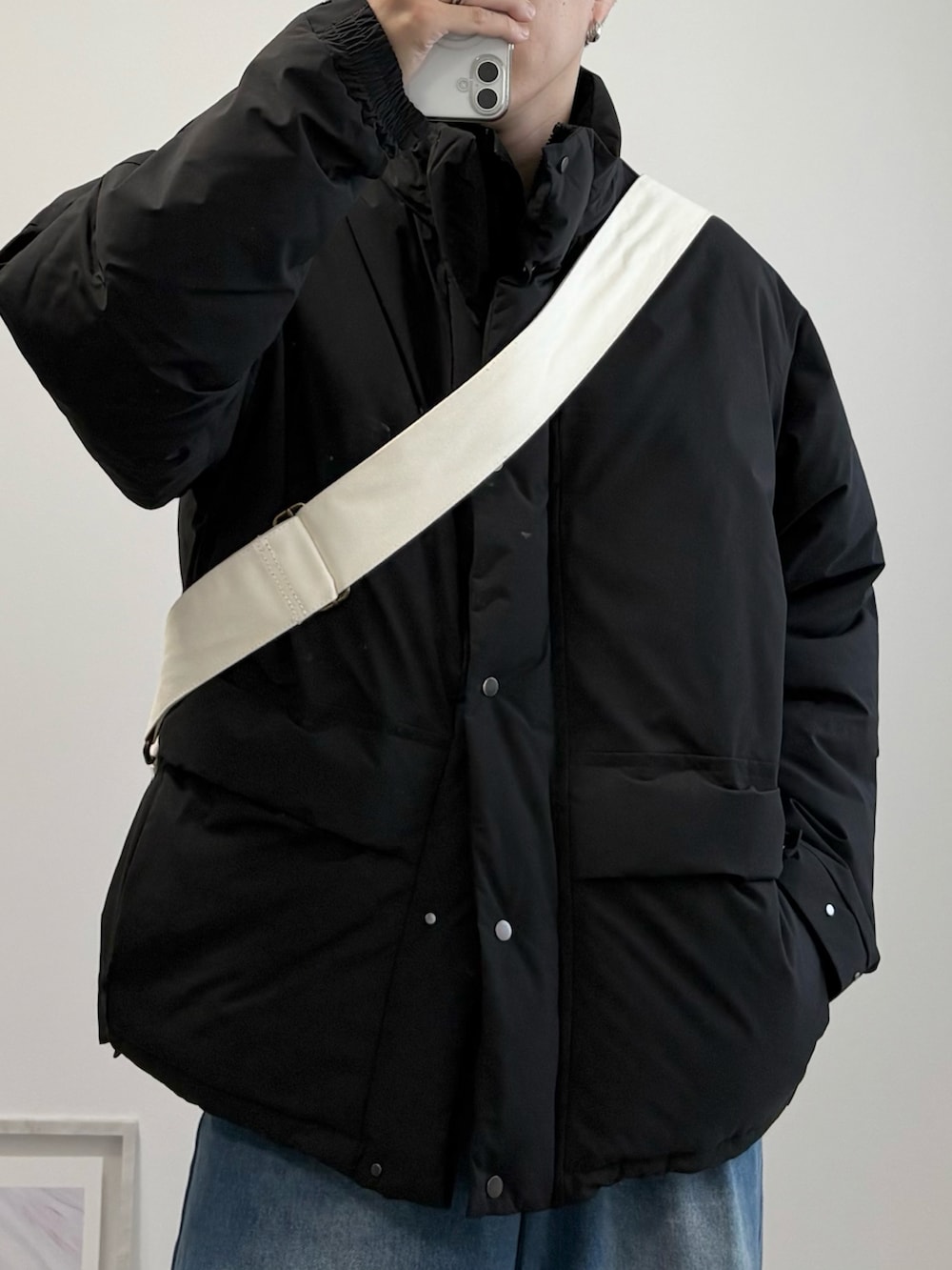 ブラック系のダウンジャケット/コート、ベージュ系のショルダーバッグ、ブルー系のデニムパンツを着用したメンズの冬コーディネートの3枚目の写真