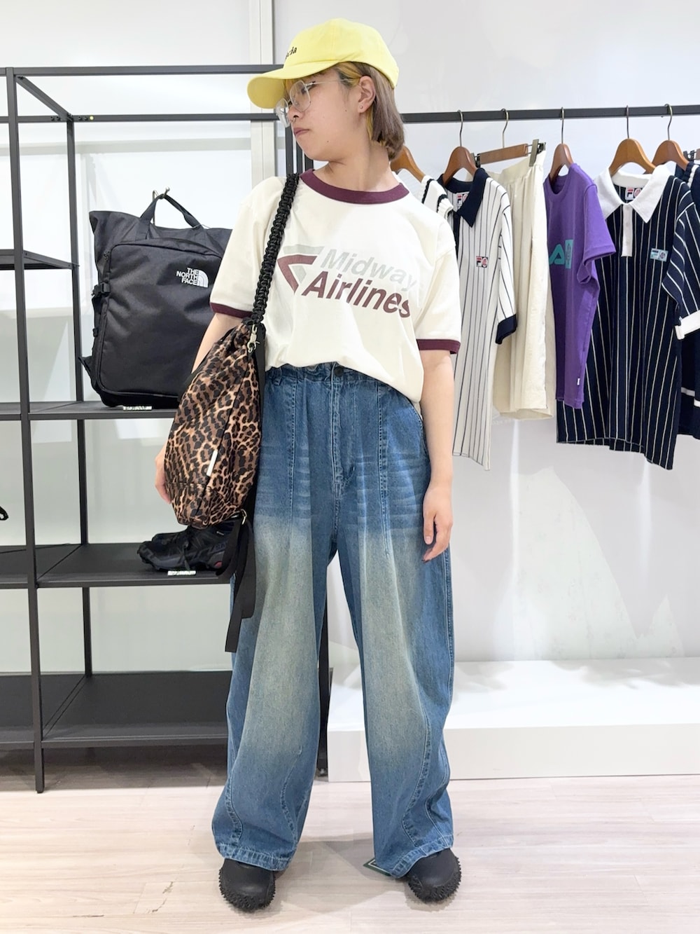 ブラウン系のトートバッグ、ブルー系のデニムパンツ、ブラック系のスニーカーを着用したレディースの夏コーディネートの2枚目の写真