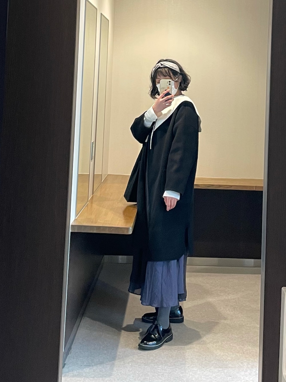 ブラック系のノーカラーコート、ホワイト系のシャツ/ブラウス、ブルー系のスカートを着用したレディースの冬コーディネートの2枚目の写真