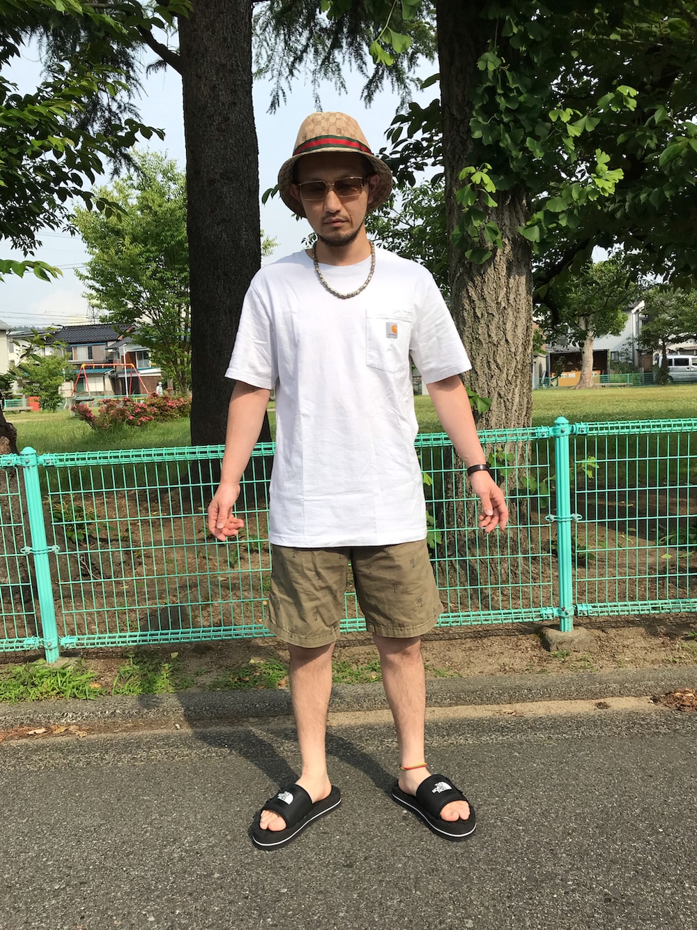 ホワイト系のTシャツ/カットソー、グリーン系のパンツ、ブラック系のサンダルを着用したメンズの夏コーディネートの2枚目の写真