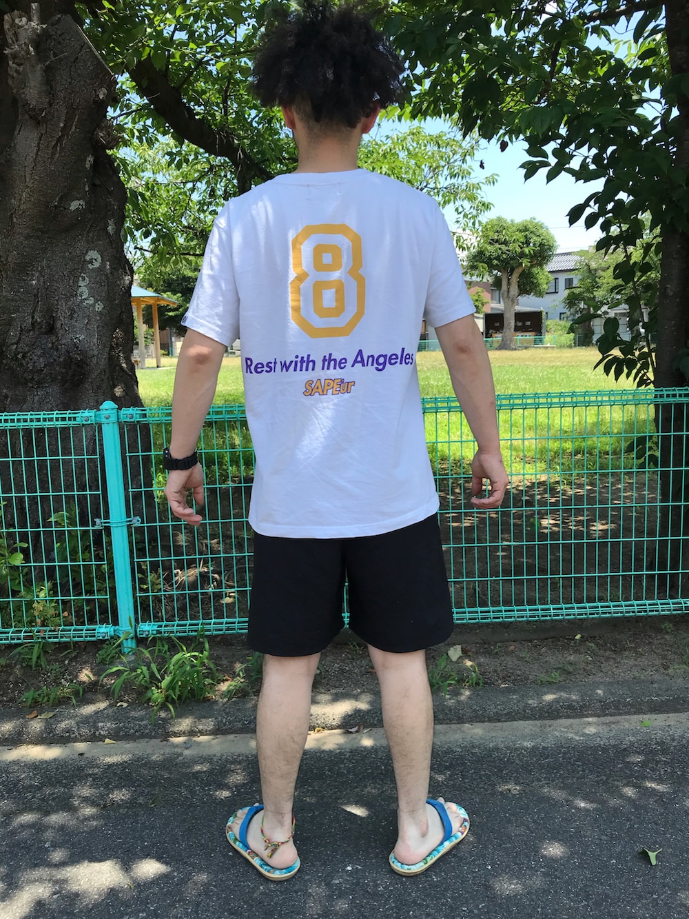 ホワイト系のTシャツ/カットソー、ブラック系のその他パンツ、ブルー系のビーチサンダルを着用したメンズの夏コーディネートの2枚目の写真