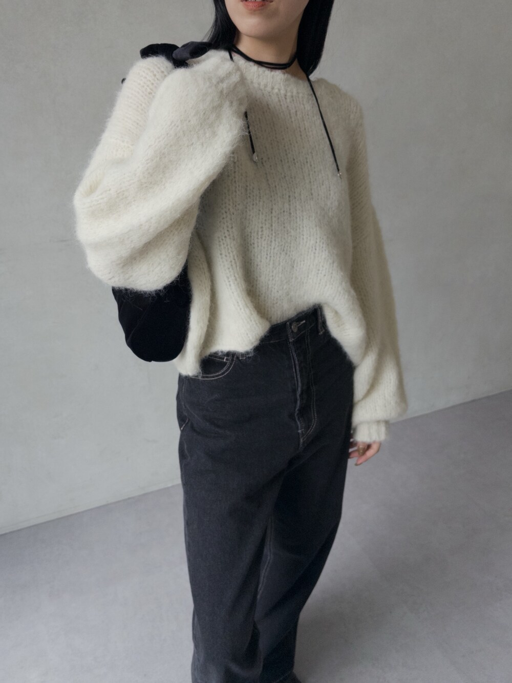 ブラック系のデニムパンツ、ホワイト系のニット/セーター、ブラック系のショルダーバッグを着用したレディースの秋コーディネートの2枚目の写真