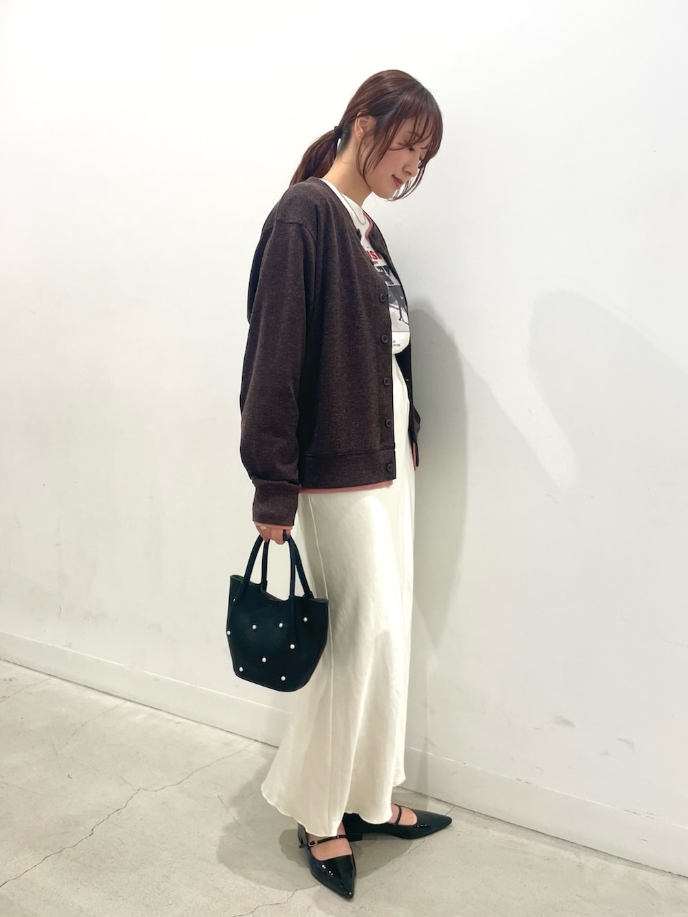 ブラック系のパンプス、ブラック系のハンドバッグ、ホワイト系のスカートを着用したレディースの冬コーディネートの2枚目の写真