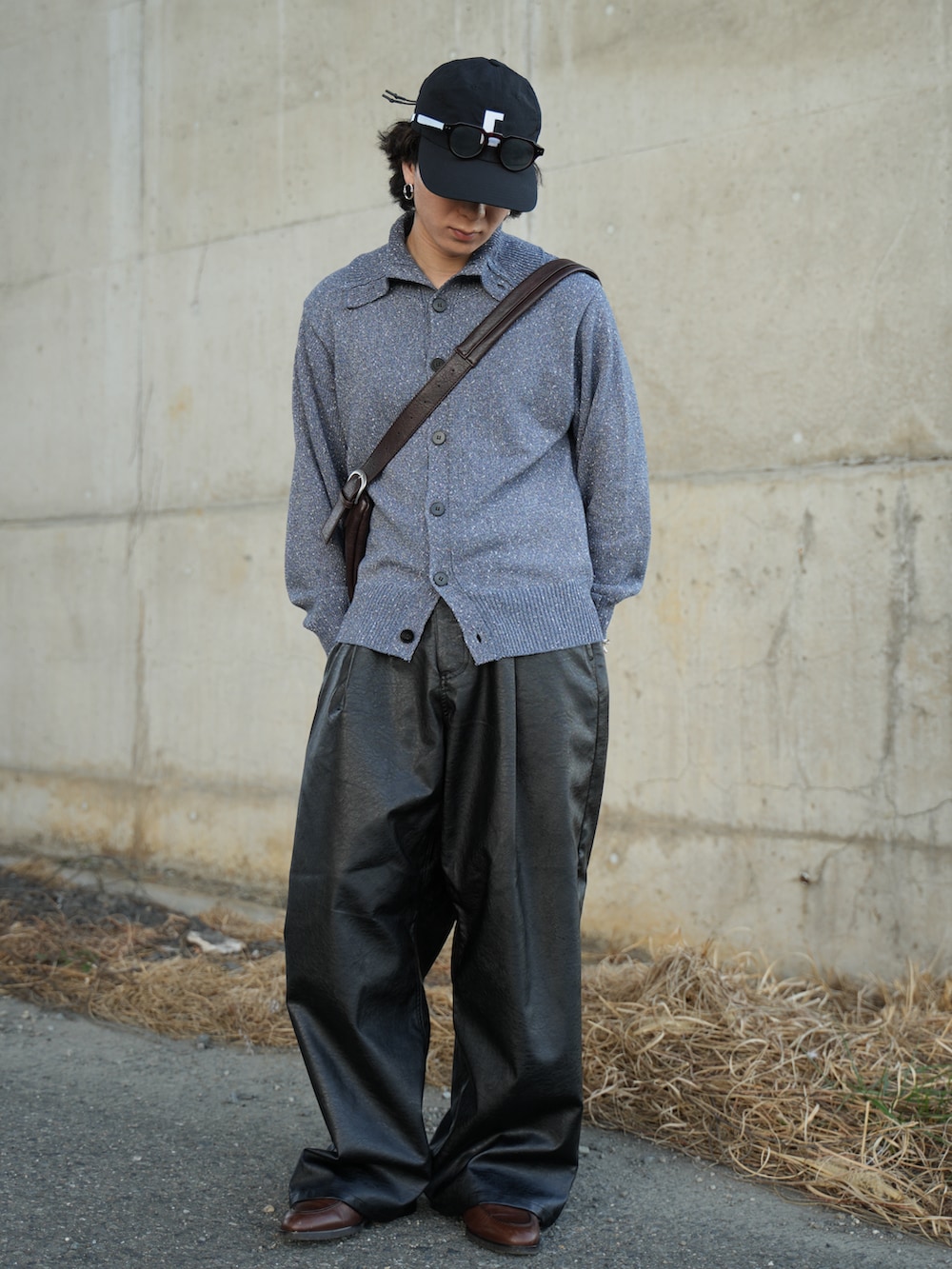 ブルー系のニット/セーター、ブラック系のスラックス、ブラウン系のショルダーバッグを着用したメンズの春コーディネートの2枚目の写真