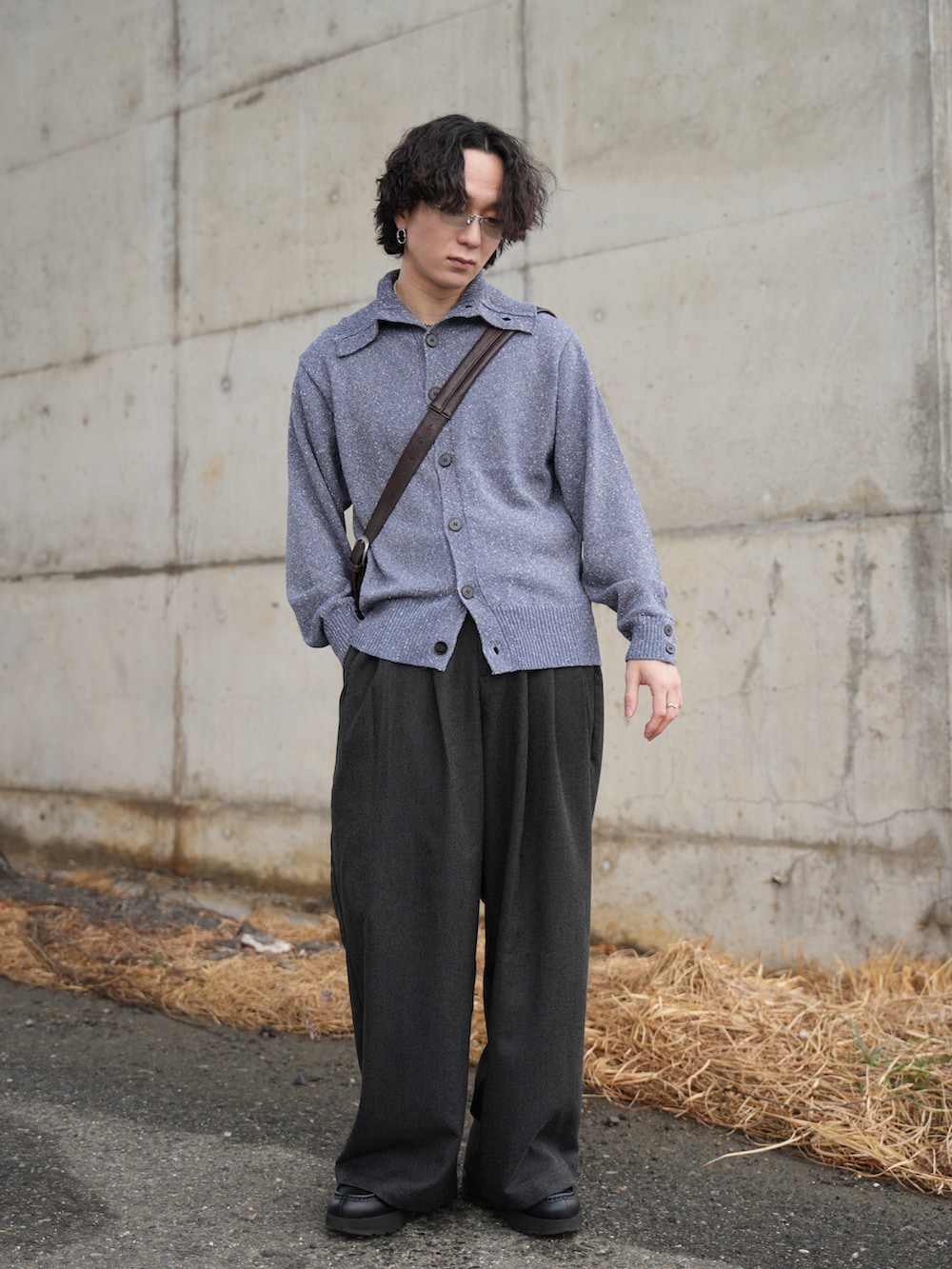 ブルー系のニット/セーター、ブラック系のスラックス、ブラウン系のショルダーバッグを着用したメンズの春コーディネートの2枚目の写真