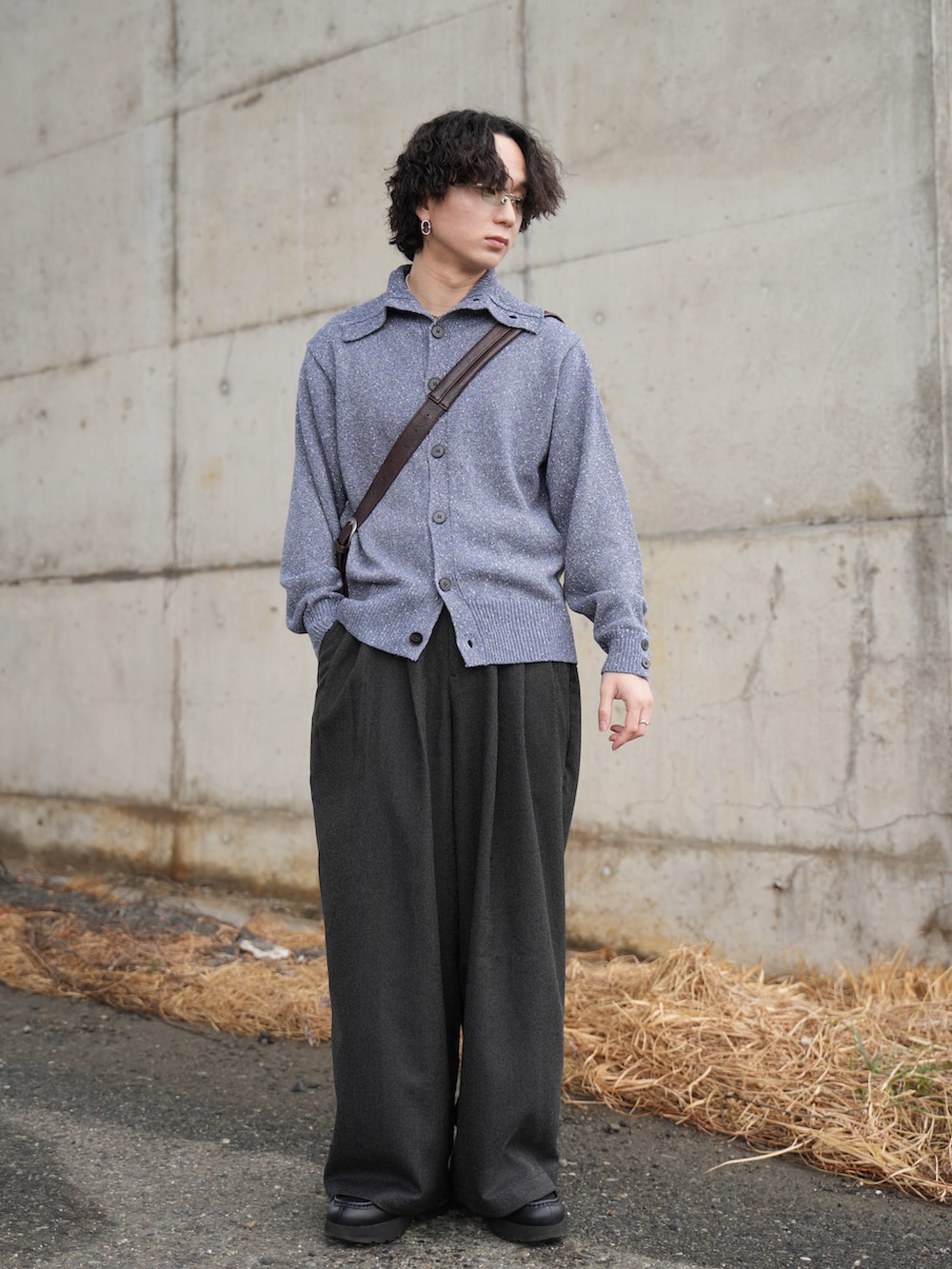 ブルー系のニット/セーター、ブラック系のスラックス、ブラウン系のショルダーバッグを着用したメンズの春コーディネートの3枚目の写真