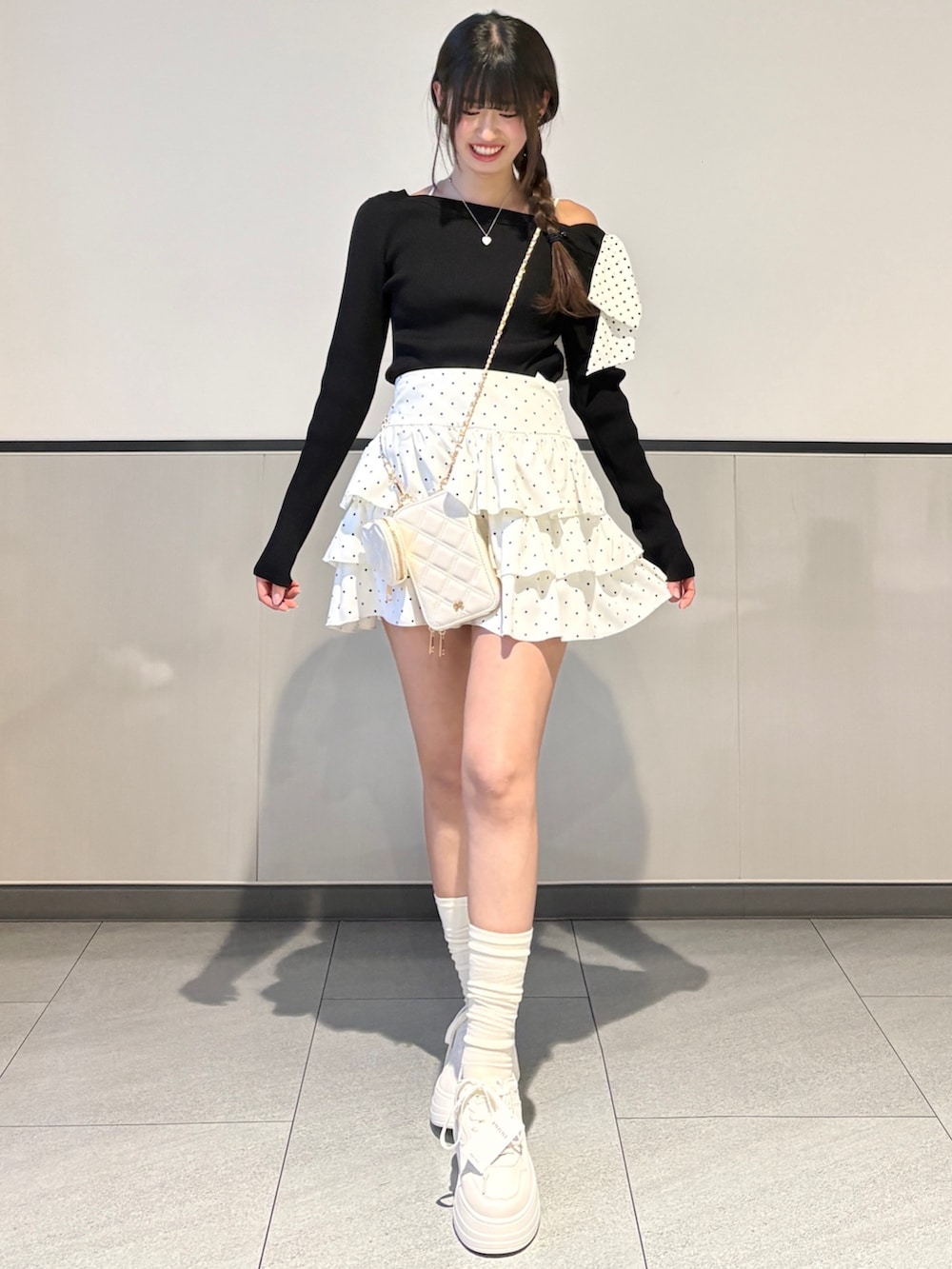 ブラック系のニット/セーター、ホワイト系のスカート、ホワイト系のスニーカーを着用したレディースの春コーディネートの2枚目の写真