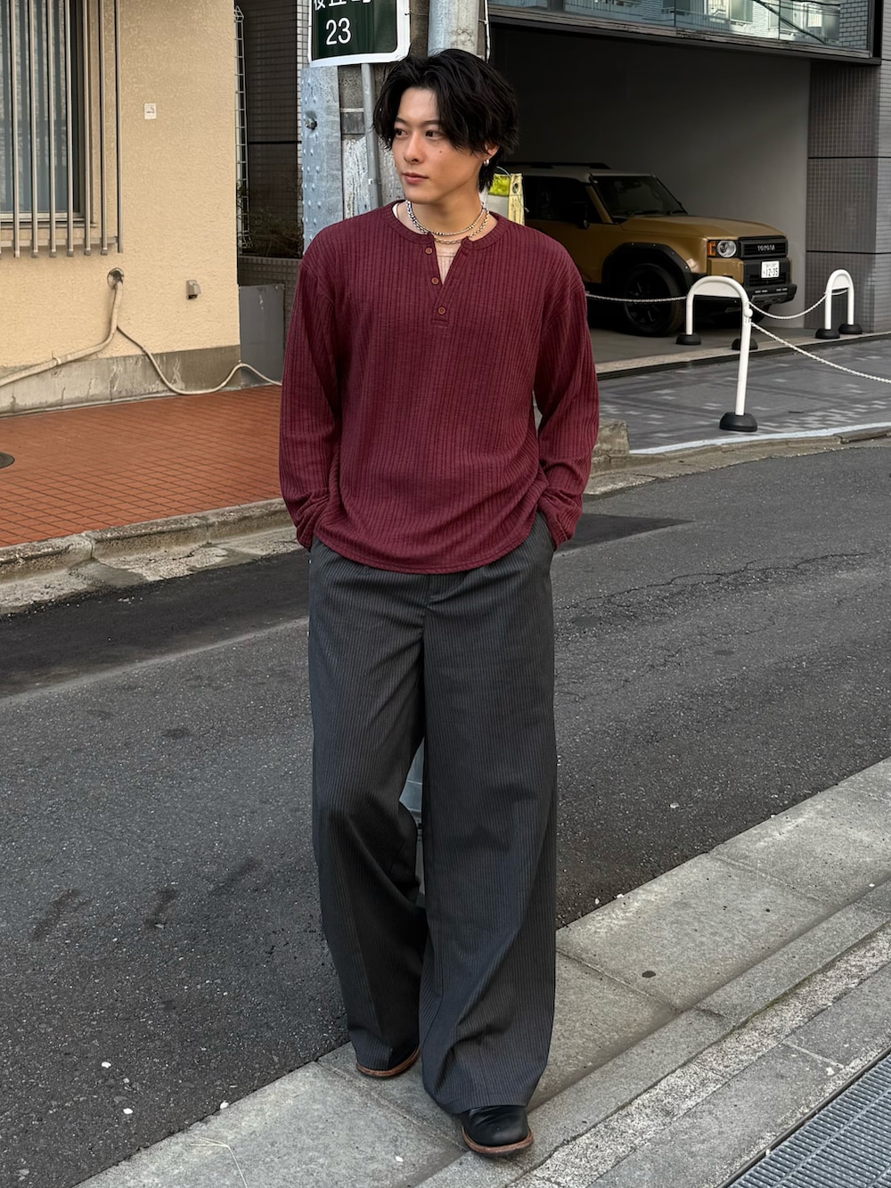 レッド系のTシャツ/カットソー、グレー系のスラックス、ブラック系のブーツを着用したメンズの春コーディネートの2枚目の写真