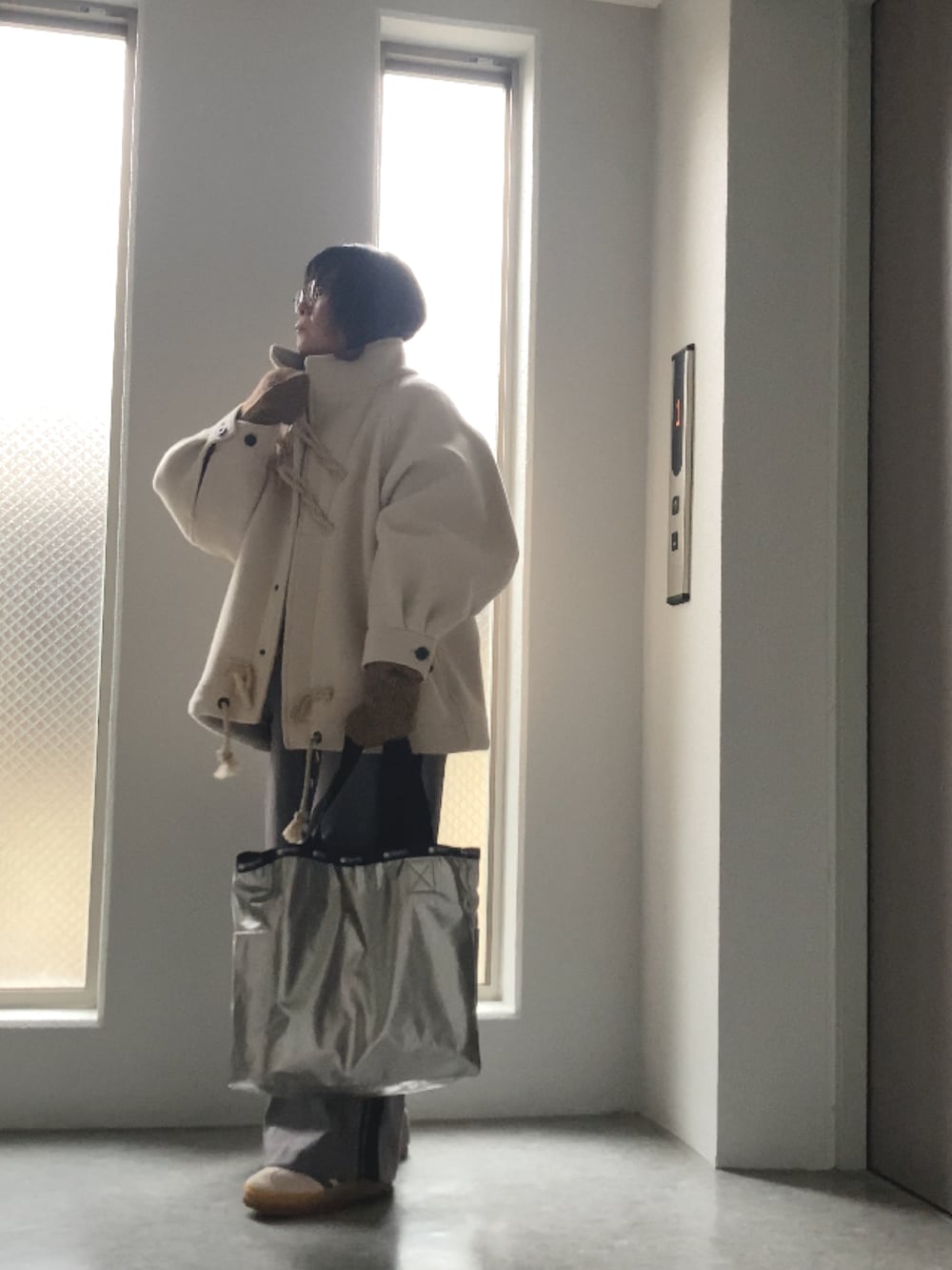 ベージュ系のベスト、グレー系のカーディガン/ボレロ、ホワイト系のダッフルコートを着用したレディースの冬コーディネートの2枚目の写真