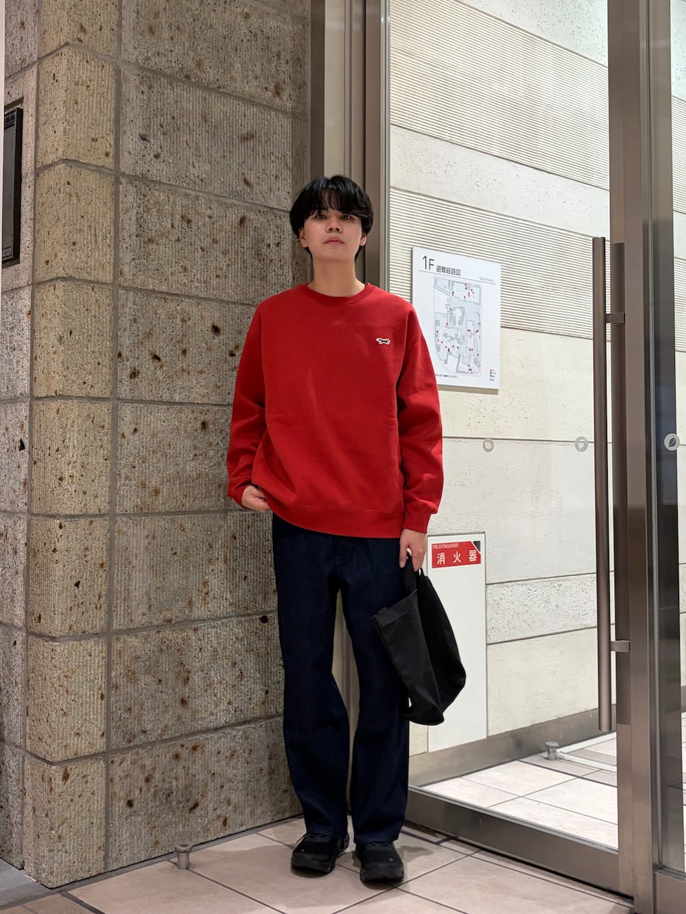 レッド系のスウェット、ブラック系のショルダーバッグ、ブルー系のデニムパンツを着用したメンズの冬コーディネートの2枚目の写真