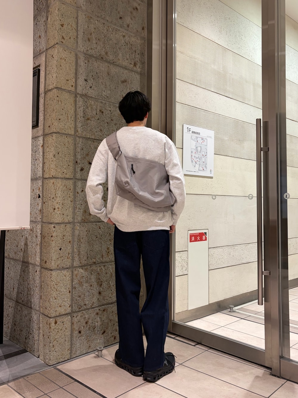 グレー系のスウェット、グレー系のショルダーバッグ、ブルー系のデニムパンツを着用したメンズの冬コーディネートの3枚目の写真