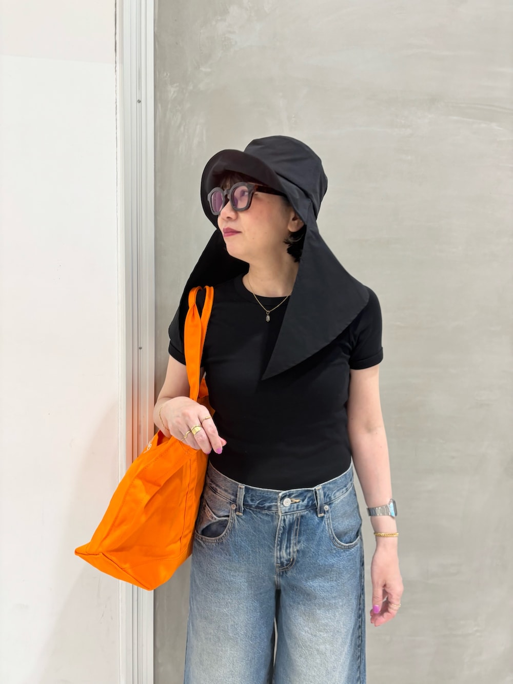 ブラック系のTシャツ/カットソー、オレンジ系のトートバッグ、ブルー系のデニムパンツを着用したレディースの春コーディネートの2枚目の写真