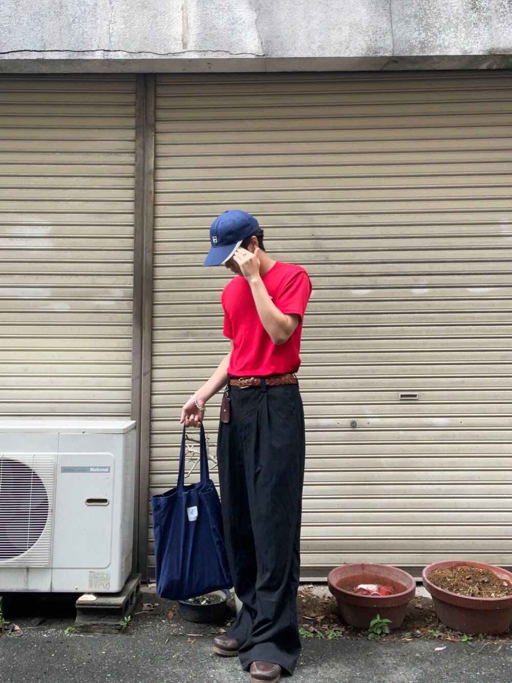 レッド系のTシャツ/カットソー、ブラック系のスラックス、ブラウン系のモカシン/デッキシューズを着用したメンズの秋コーディネートの2枚目の写真