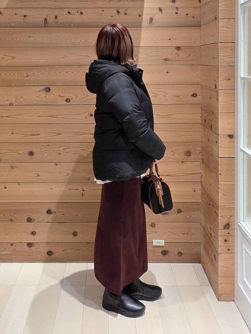 ブラック系のダウンジャケット/コート、レッド系のスカート、ブラック系のブーツを着用したレディースの冬コーディネートの2枚目の写真