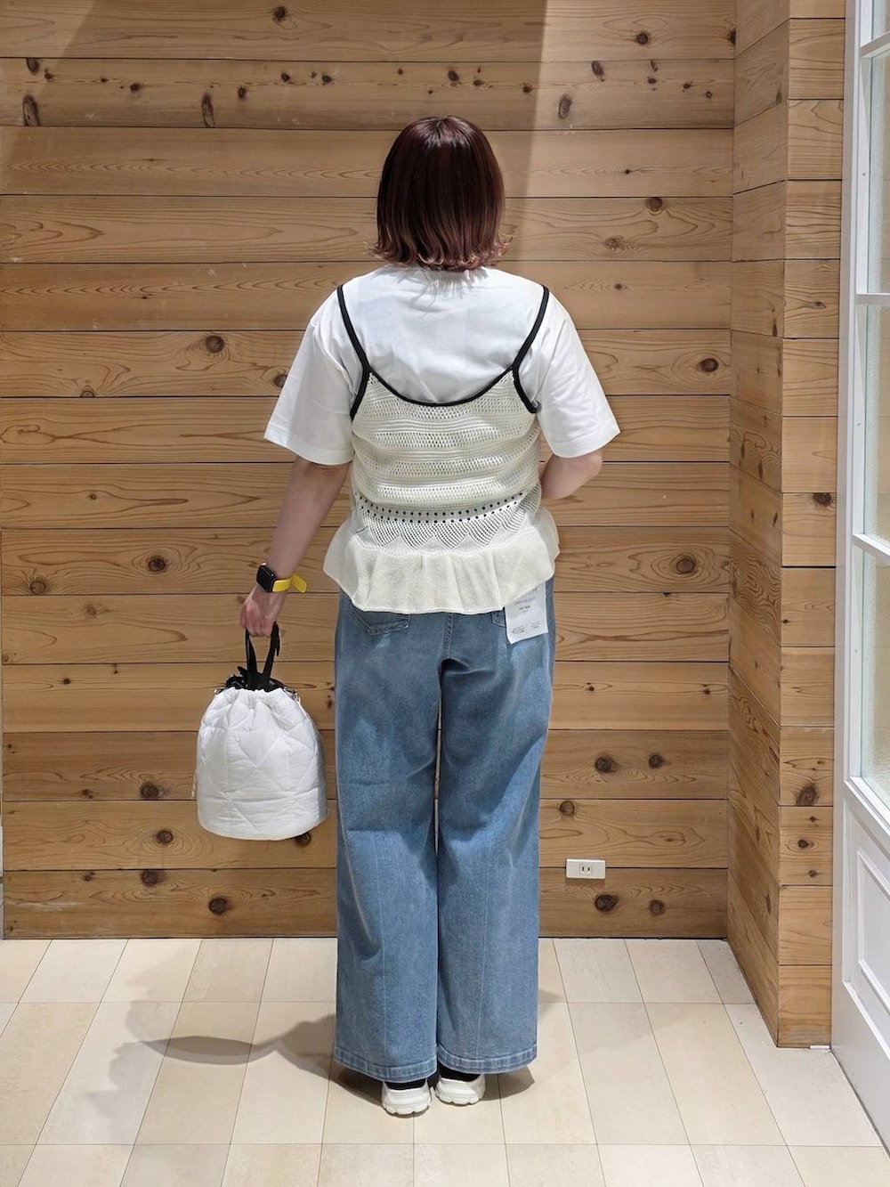 ブラック系のスニーカー、ホワイト系のハンドバッグ、ブルー系のデニムパンツを着用したレディースの春コーディネートの3枚目の写真