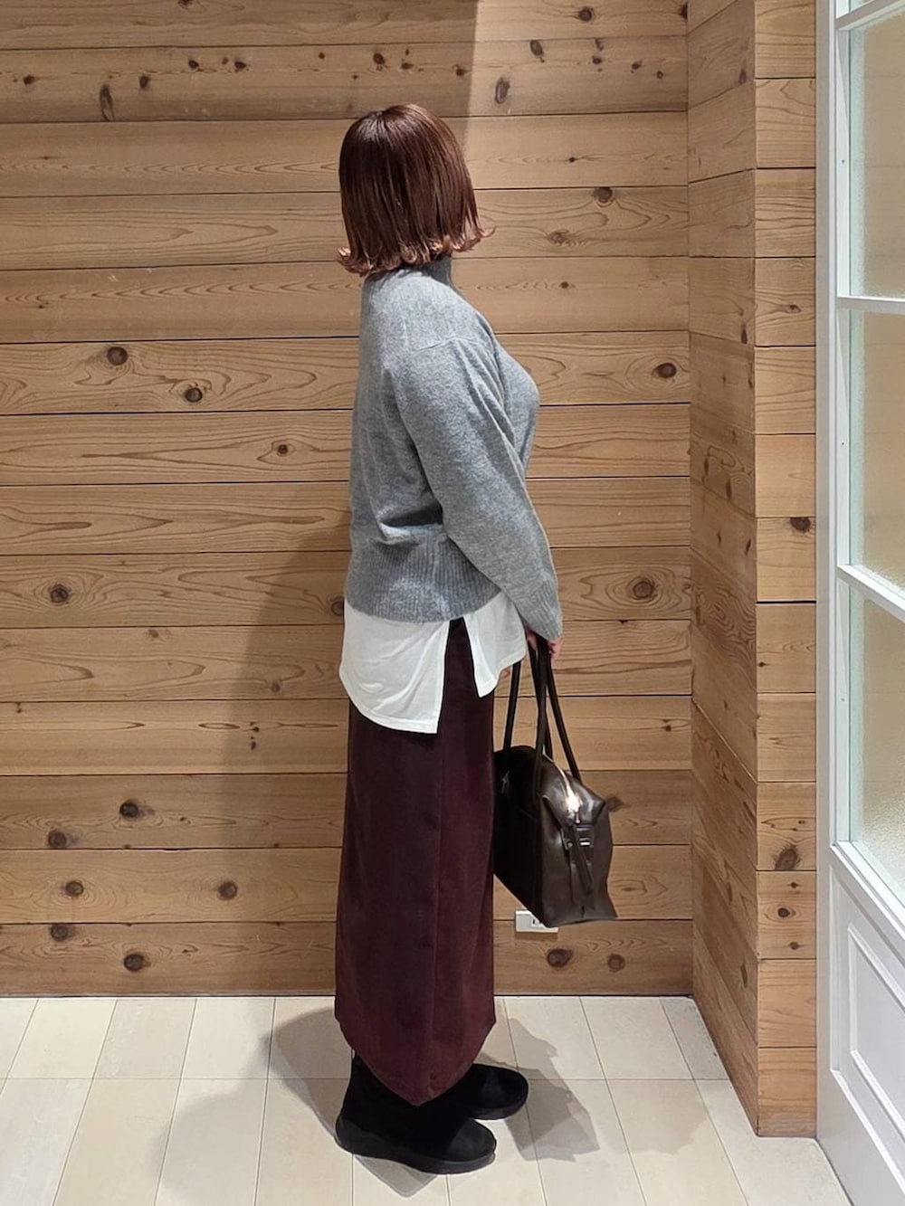 ブラウン系のボストンバッグ、ブラウン系のチェスターコート、レッド系のスカートを着用したレディースの冬コーディネートの2枚目の写真