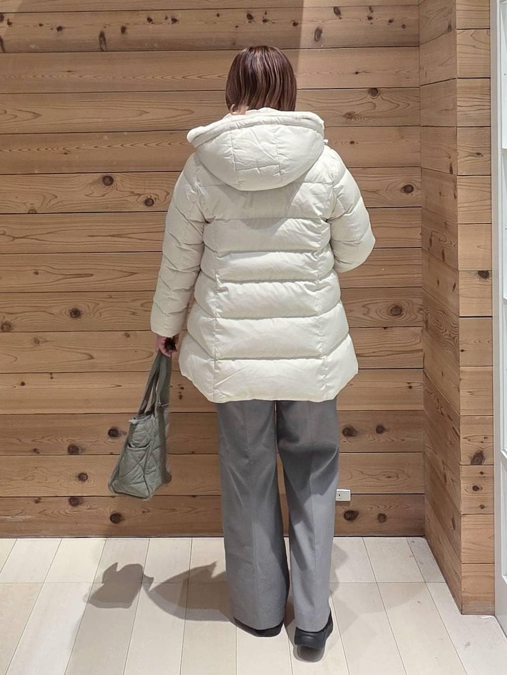 グリーン系のトートバッグ、ベージュ系のダウンジャケット/コート、ブラック系のブーツを着用したレディースの冬コーディネートの3枚目の写真