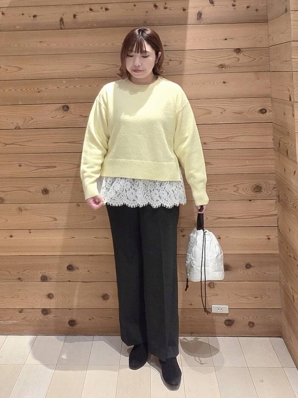 グレー系のチェスターコート、ホワイト系のハンドバッグ、イエロー系のニット/セーターを着用したレディースの冬コーディネートの4枚目の写真