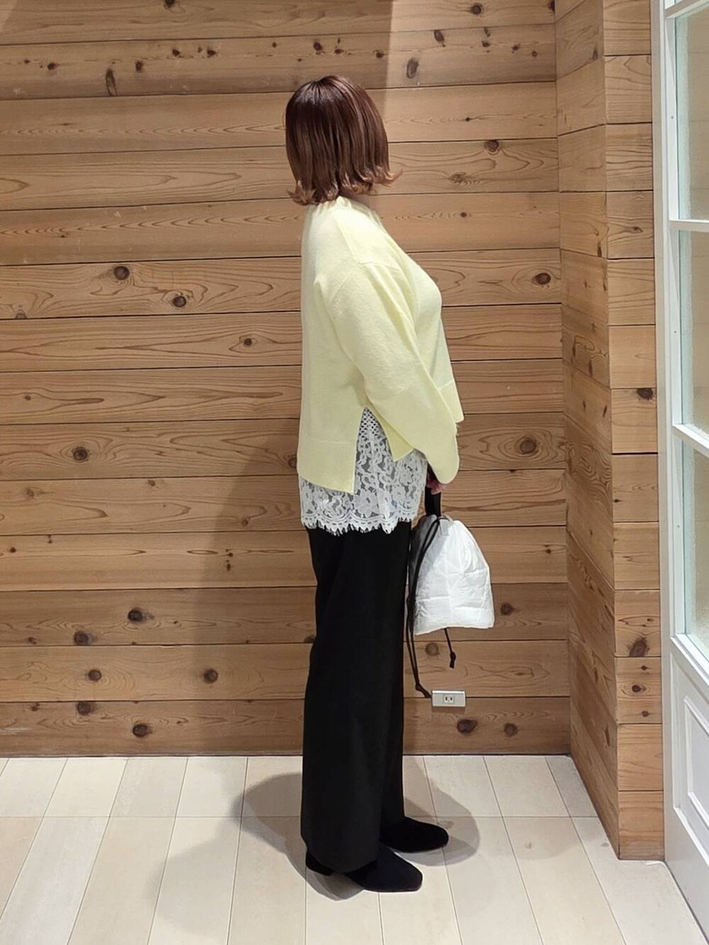 グレー系のチェスターコート、ホワイト系のハンドバッグ、イエロー系のニット/セーターを着用したレディースの冬コーディネートの2枚目の写真