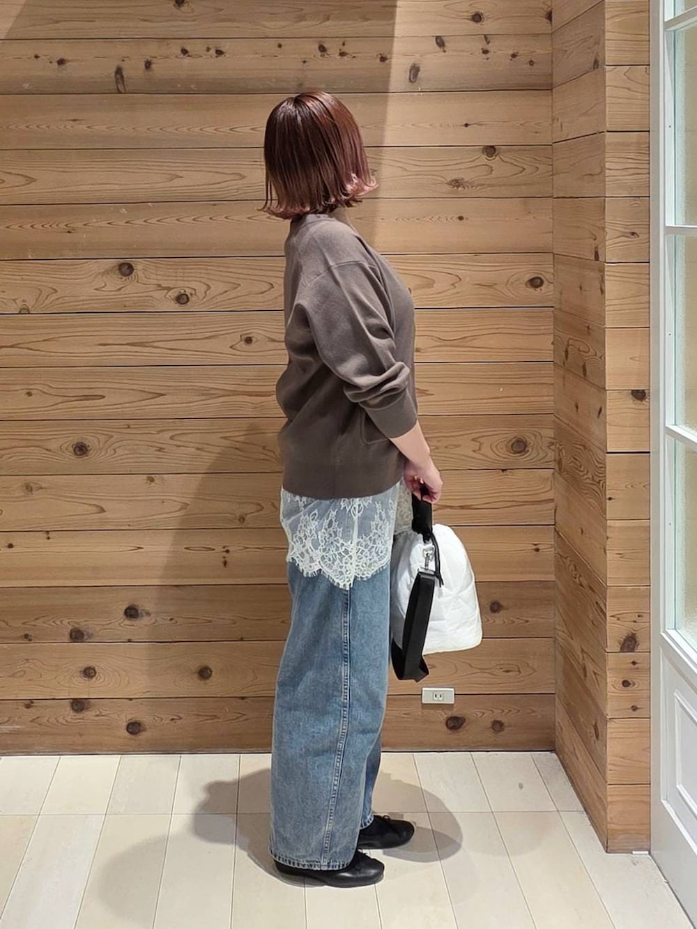 ブラック系のバレエシューズ、ホワイト系のハンドバッグ、ブルー系のデニムパンツを着用したレディースの春コーディネートの2枚目の写真