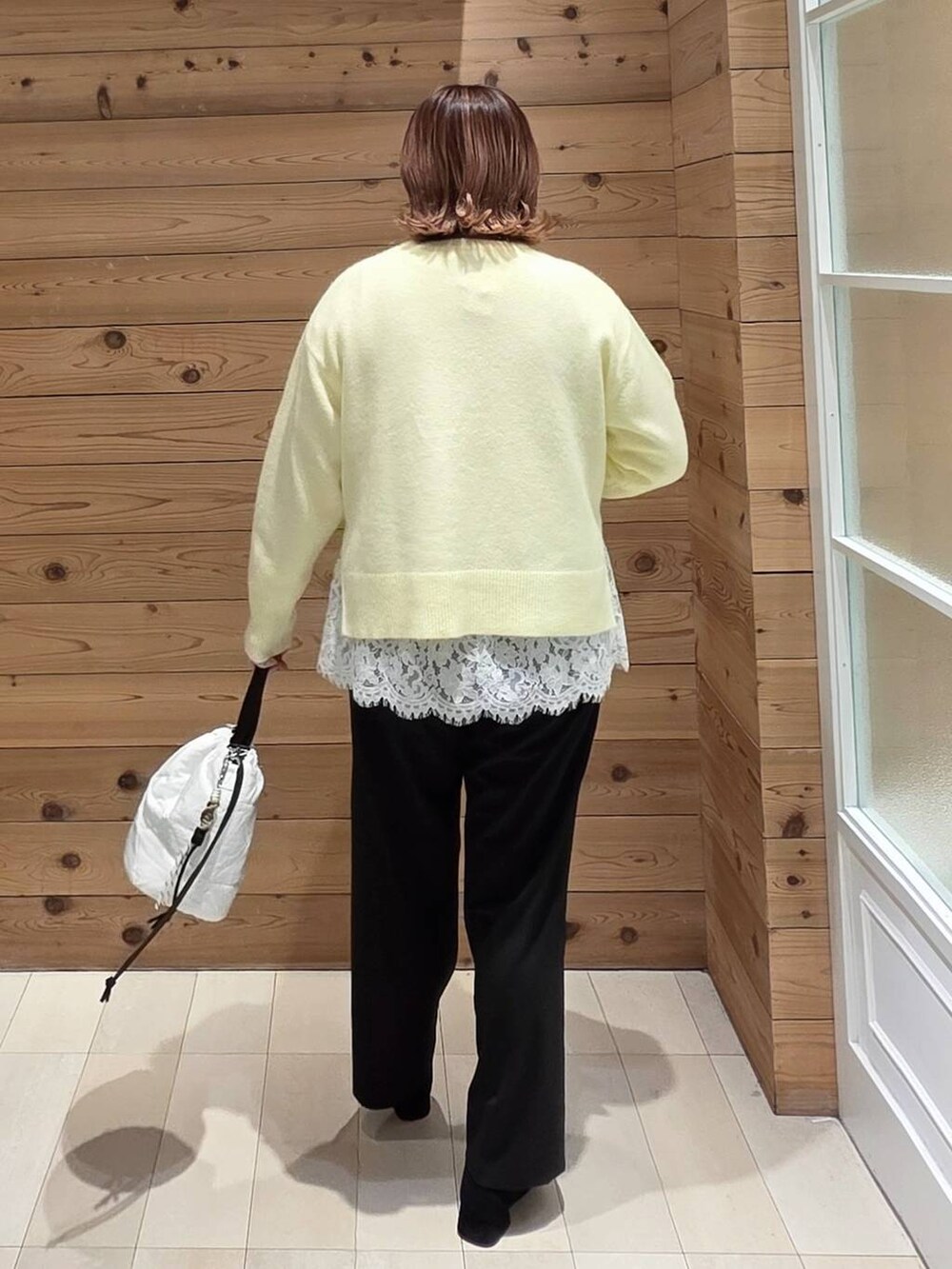 グレー系のチェスターコート、ホワイト系のハンドバッグ、イエロー系のニット/セーターを着用したレディースの冬コーディネートの3枚目の写真