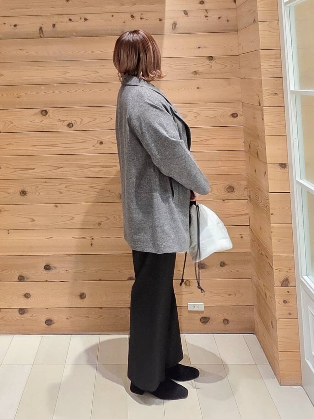 グレー系のチェスターコート、ホワイト系のハンドバッグ、イエロー系のニット/セーターを着用したレディースの冬コーディネートの2枚目の写真