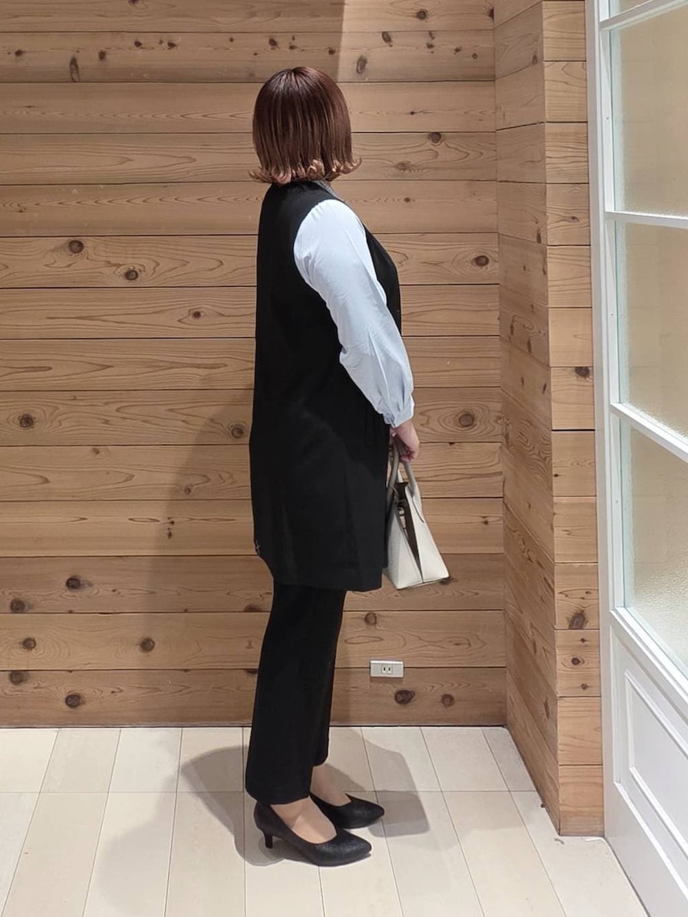 ホワイト系のショルダーバッグ、ブラック系のパンプス、ブラック系のスラックスを着用したレディースの冬コーディネートの2枚目の写真