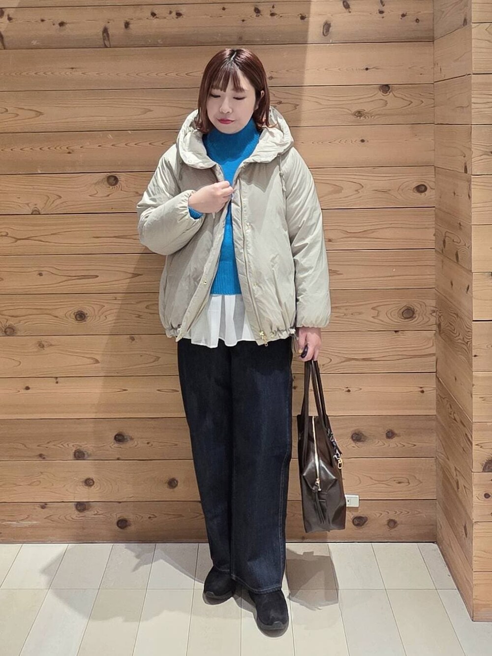 ベージュ系のダウンジャケット/コート、ブラウン系のボストンバッグ、ブルー系のデニムパンツを着用したレディースの冬コーディネートの4枚目の写真