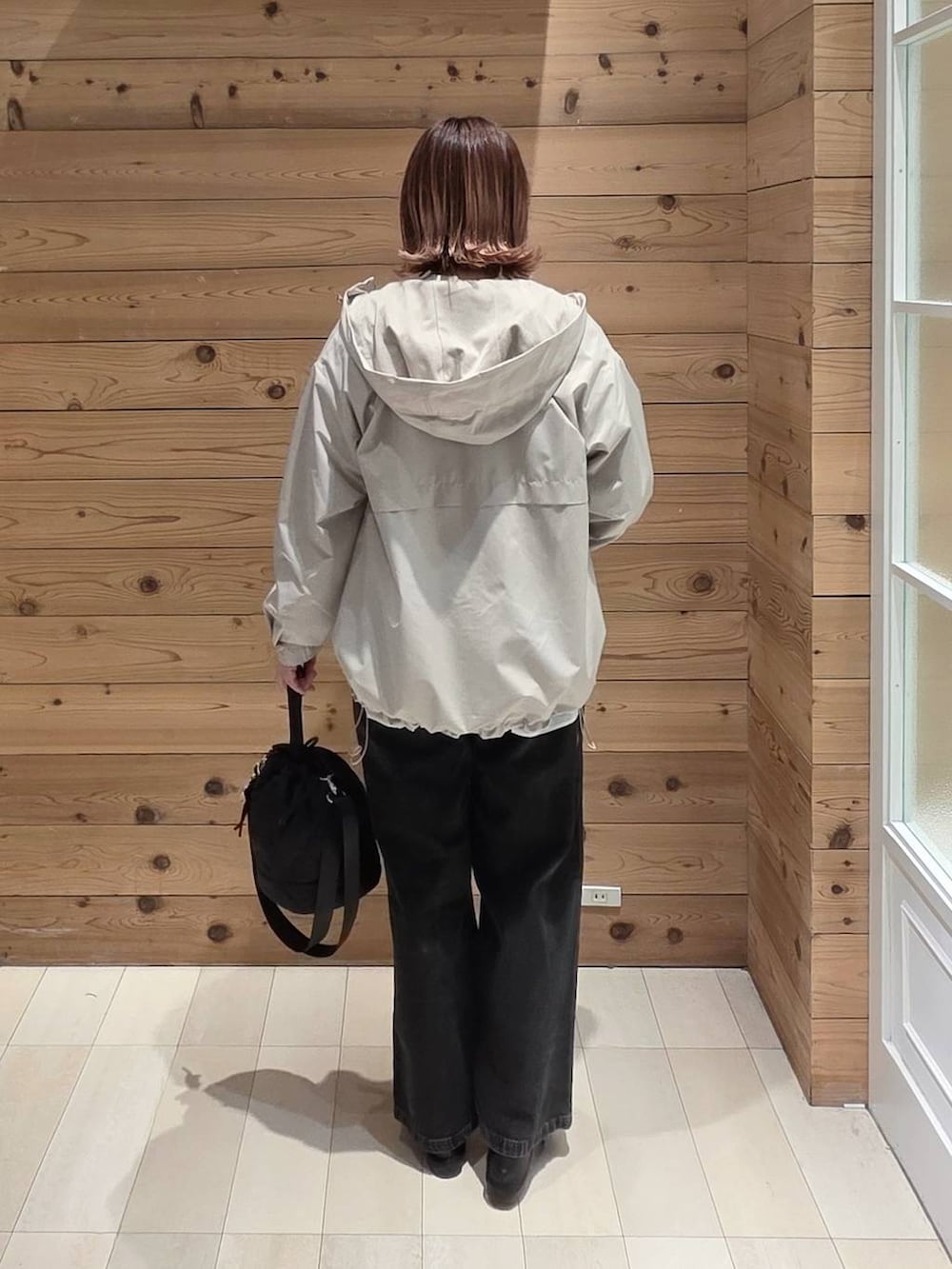 ブラック系のデニムパンツ、ブラック系のハンドバッグ、ベージュ系のマウンテンパーカーを着用したレディースの春コーディネートの3枚目の写真