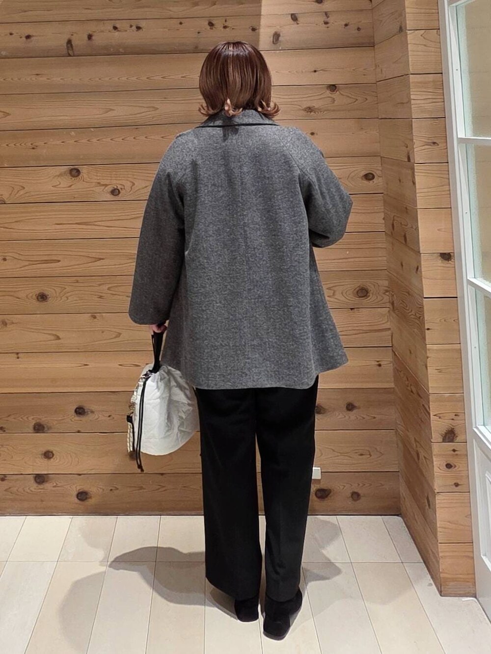 グレー系のチェスターコート、ホワイト系のハンドバッグ、イエロー系のニット/セーターを着用したレディースの冬コーディネートの3枚目の写真