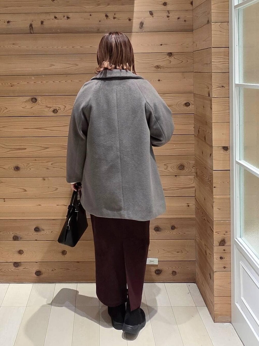 ブラック系のショルダーバッグ、ブラウン系のチェスターコート、レッド系のスカートを着用したレディースの冬コーディネートの3枚目の写真