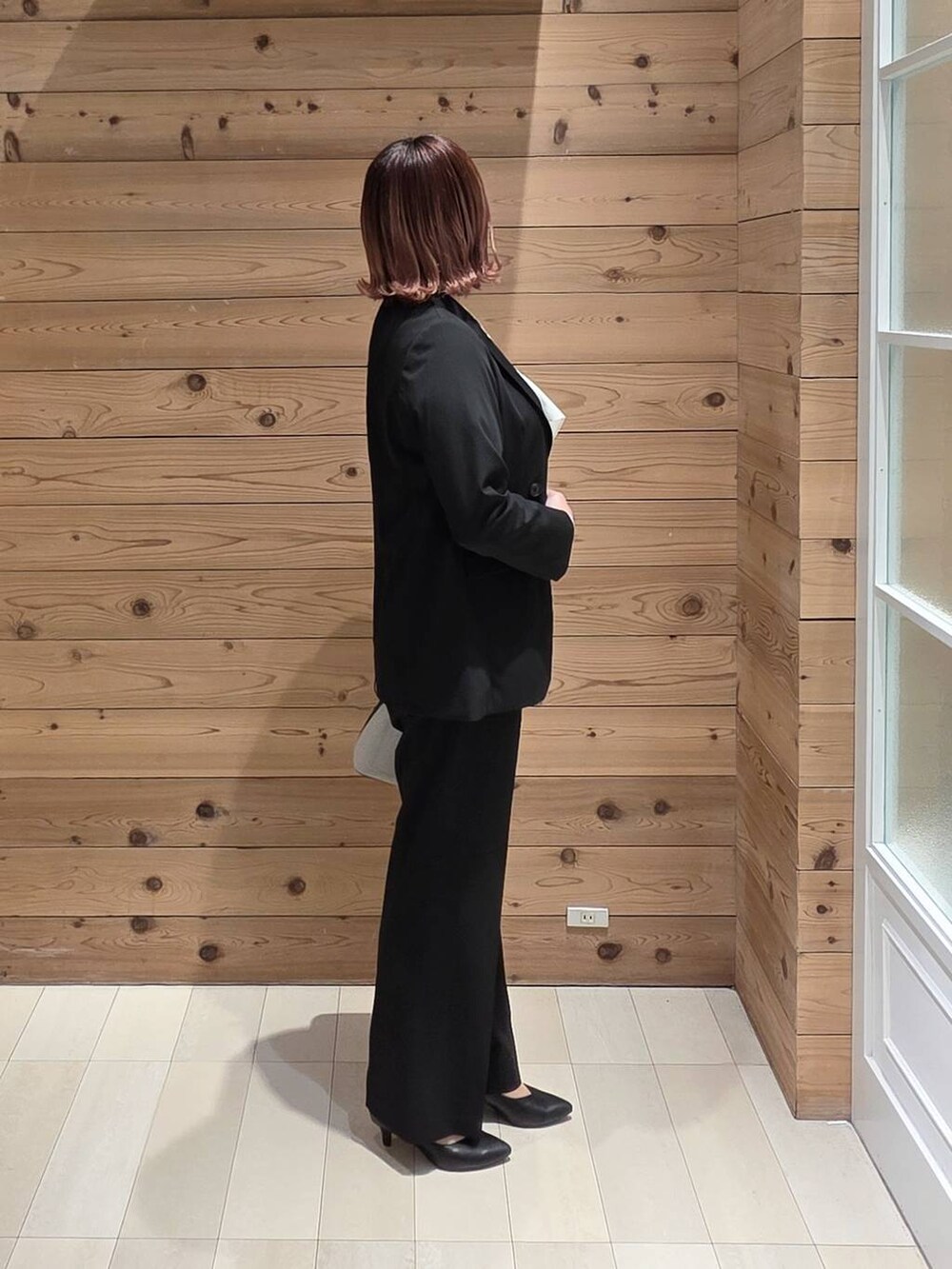 ホワイト系のショルダーバッグ、ブラック系のパンプス、ブラック系のスラックスを着用したレディースの春コーディネートの2枚目の写真