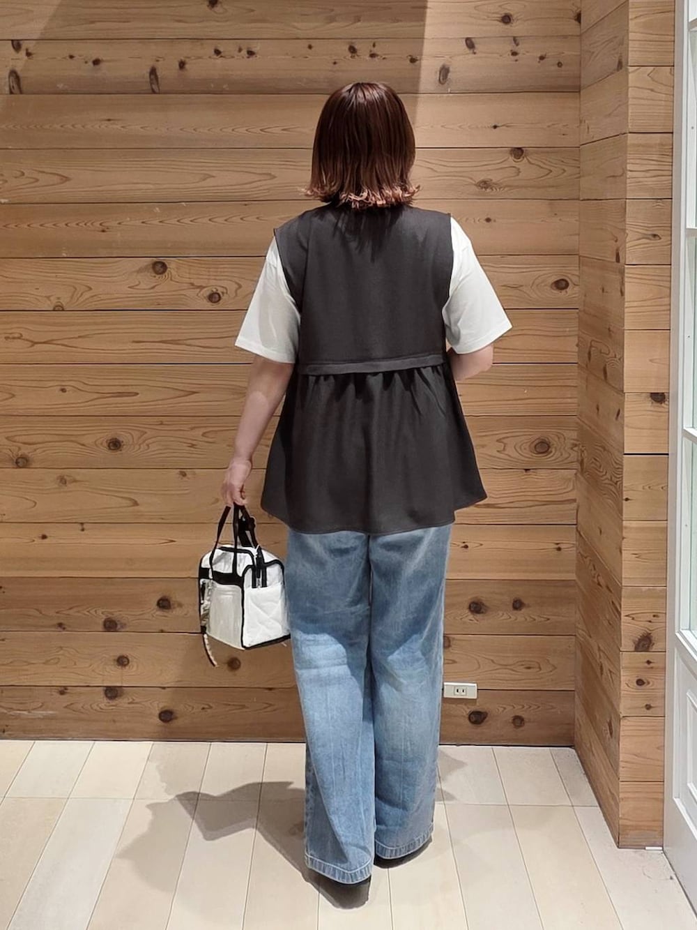 ホワイト系のボストンバッグ、グレー系のベスト、ブルー系のデニムパンツを着用したレディースの春コーディネートの3枚目の写真