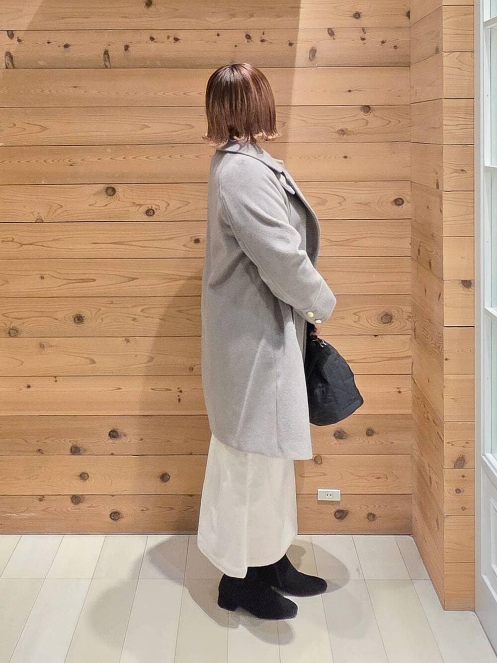 ベージュ系のチェスターコート、グレー系のスカート、ブラック系のハンドバッグを着用したレディースの冬コーディネートの2枚目の写真