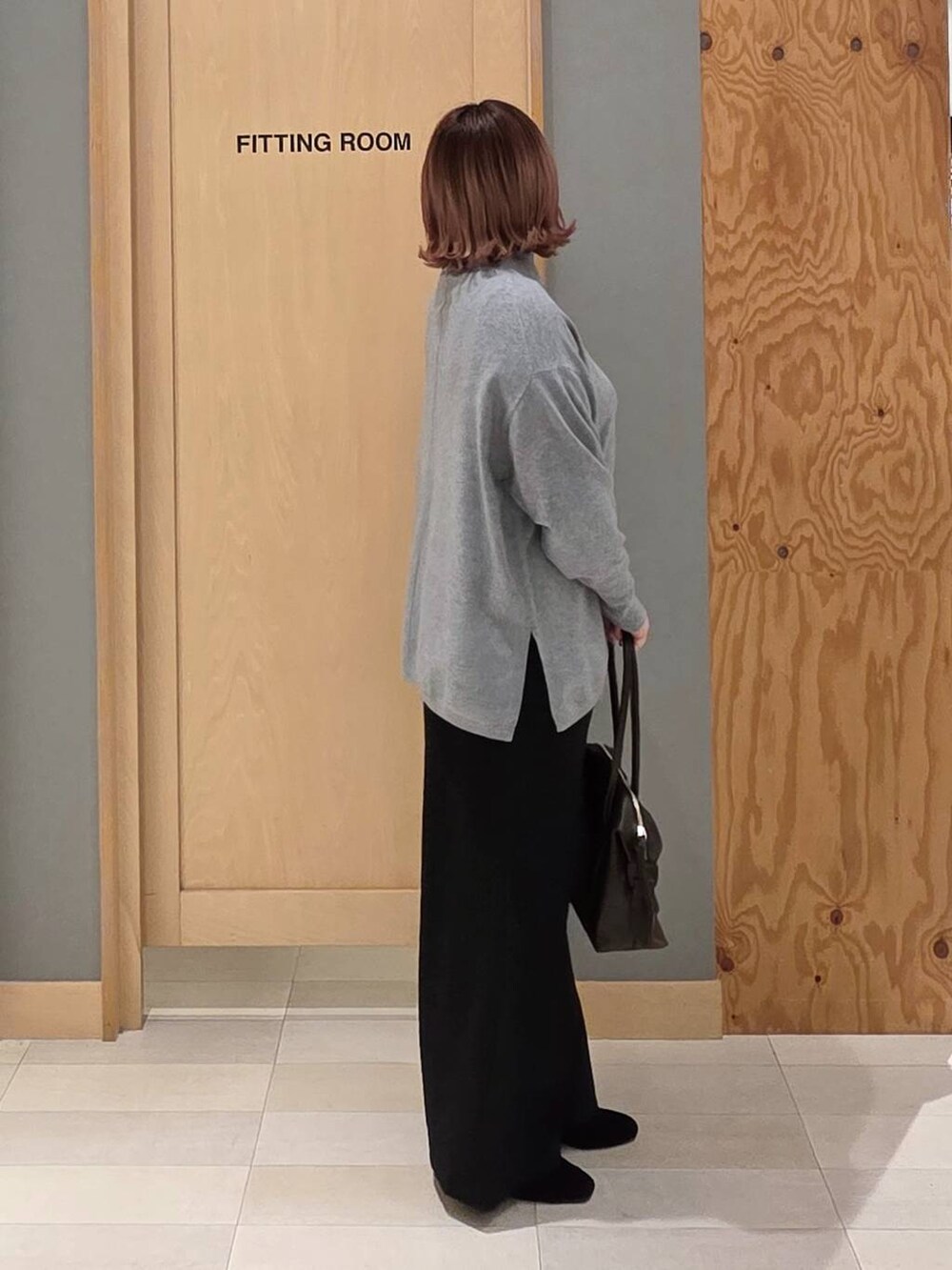 ブラウン系のボストンバッグ、ブラック系のダウンジャケット/コート、グレー系のニット/セーターを着用したレディースの冬コーディネートの2枚目の写真