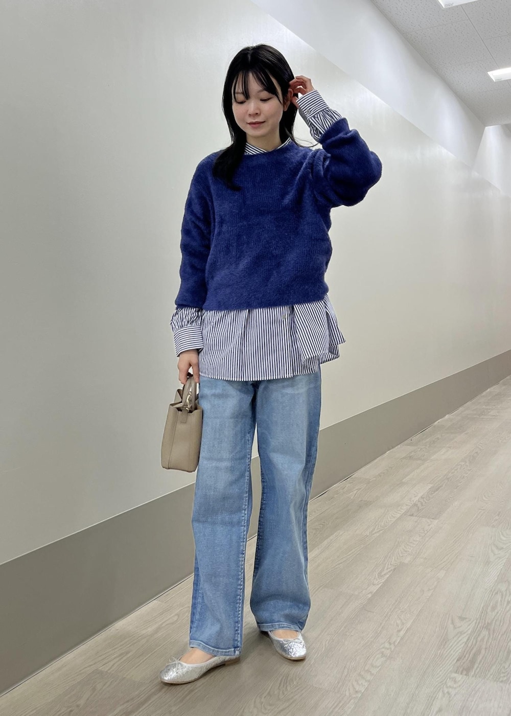 シルバー系のバレエシューズ、ブルー系のデニムパンツ、ベージュ系のショルダーバッグを着用したレディースの冬コーディネートの2枚目の写真