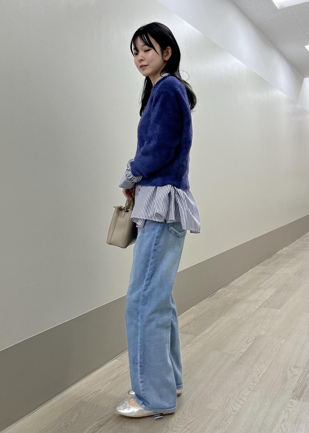シルバー系のバレエシューズ、ブルー系のデニムパンツ、ベージュ系のショルダーバッグを着用したレディースの冬コーディネートの4枚目の写真