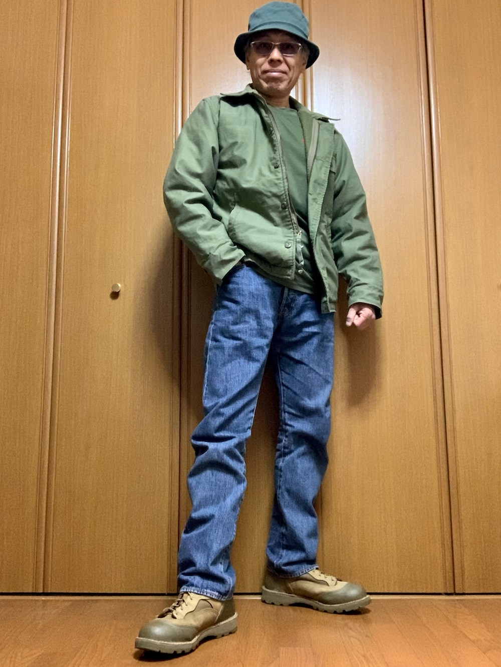 グリーン系のTシャツ/カットソー、グリーン系のミリタリージャケット、ブルー系のデニムパンツを着用したメンズの冬コーディネートの2枚目の写真