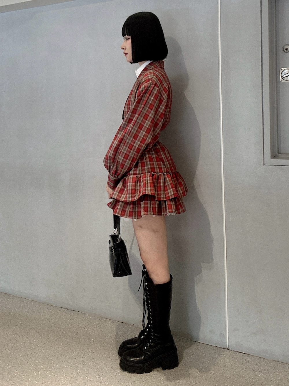 レッド系のワンピース、ブラック系のブーツ、ブラック系のハンドバッグを着用したレディースの冬コーディネートの2枚目の写真