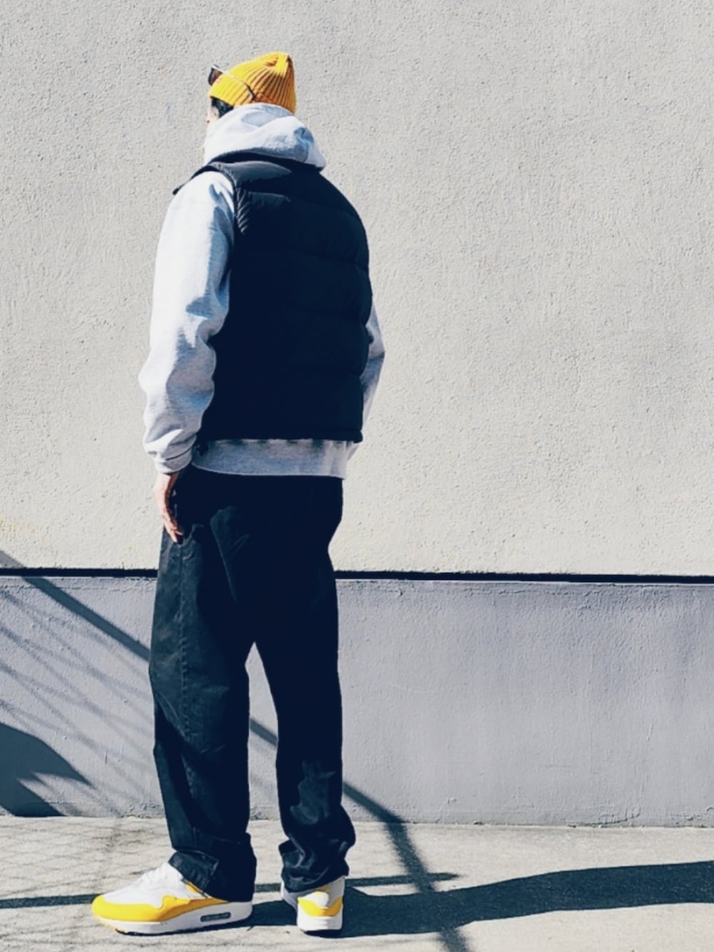 グレー系のパーカー、ブラック系のダウンベスト、ブラック系のチノパンツを着用したメンズの冬コーディネートの2枚目の写真