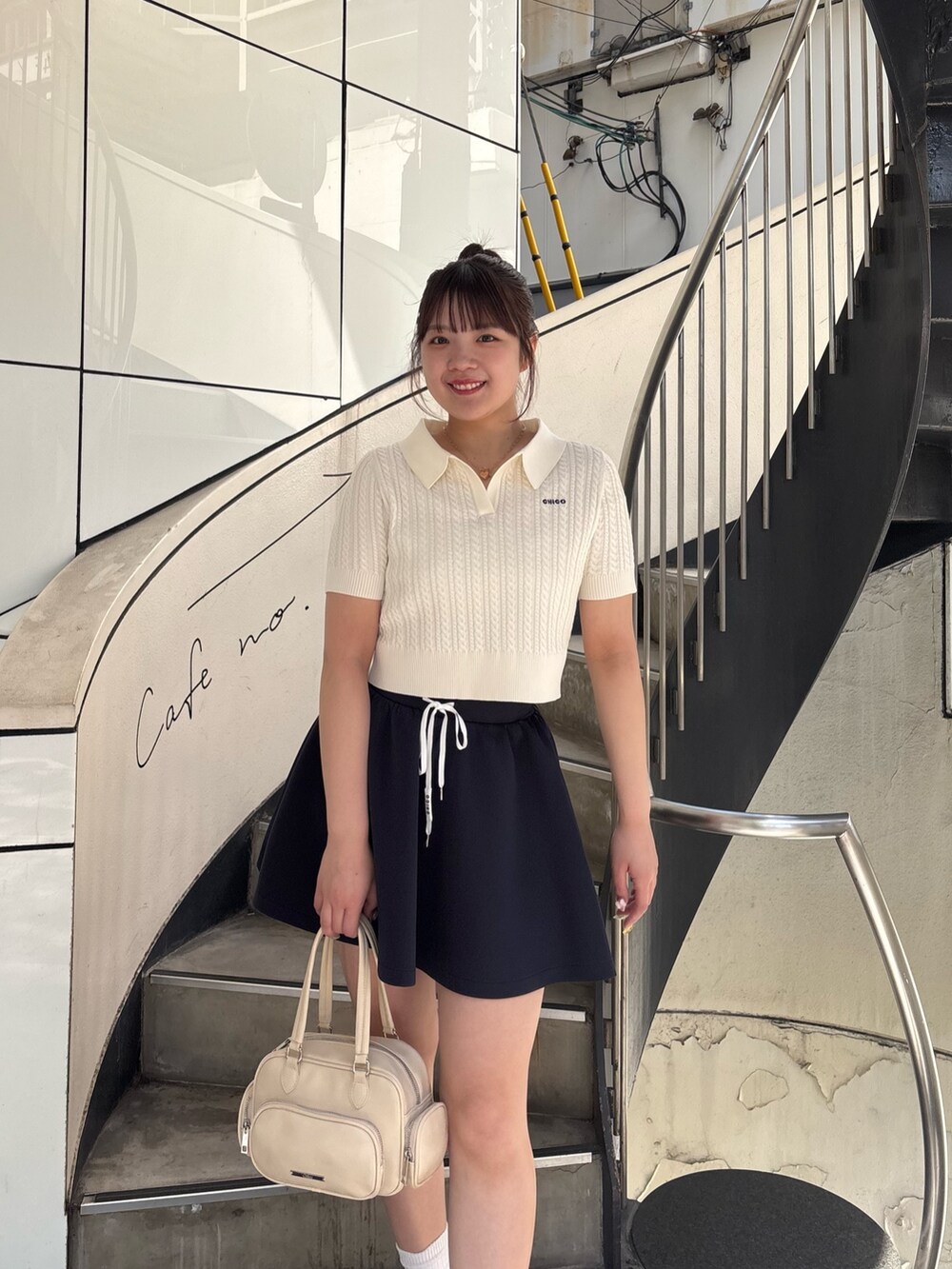 ブルー系のスカート、ホワイト系のニット/セーター、ホワイト系のボストンバッグを着用したレディースの春コーディネートの2枚目の写真