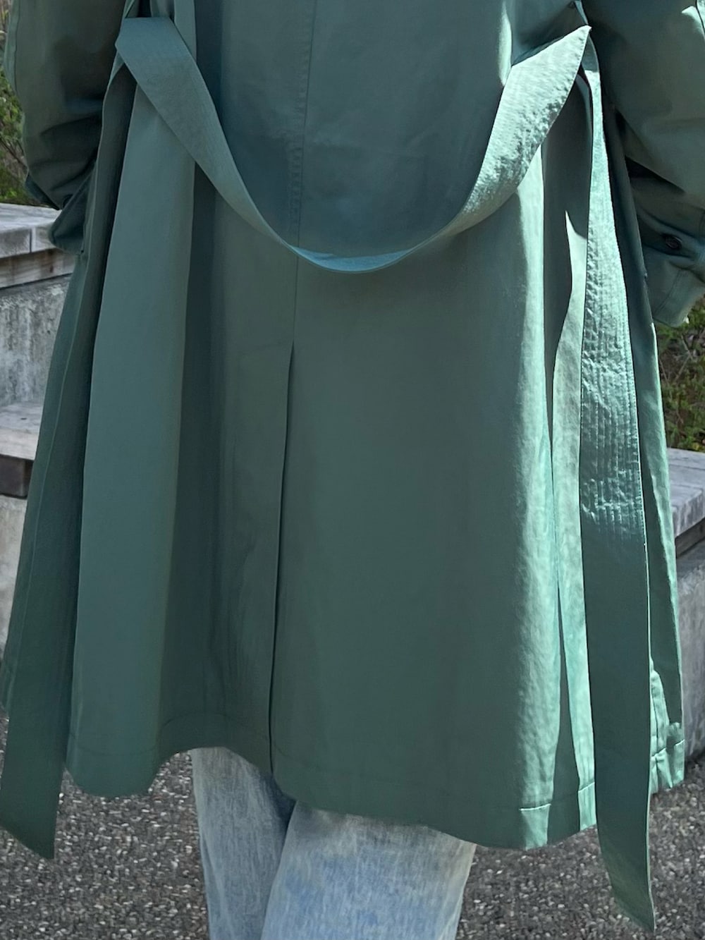 グリーン系のステンカラーコート、ベージュ系のパーカー、ホワイト系のスニーカーを着用したメンズの春コーディネートの3枚目の写真