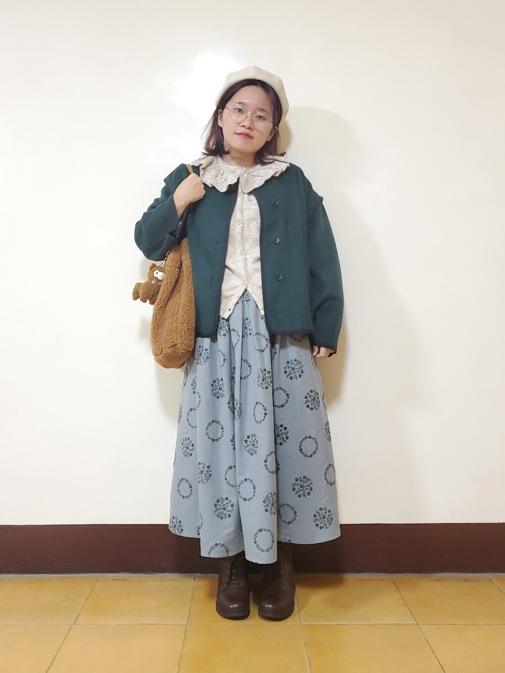 グリーン系のノーカラーコート、ホワイト系のニット/セーター、ブルー系のスカートを着用したレディースの冬コーディネートの2枚目の写真