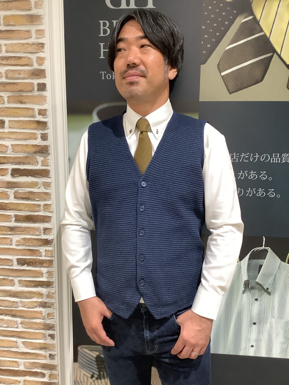 イエロー系のビジネスシャツ、ブルー系のベストを着用したメンズの秋コーディネートの2枚目の写真