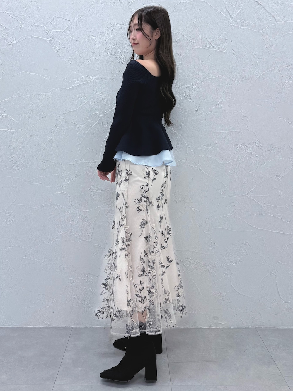 ブルー系のニット/セーター、ホワイト系のスカート、ブラック系のブーツを着用したレディースの秋コーディネートの2枚目の写真