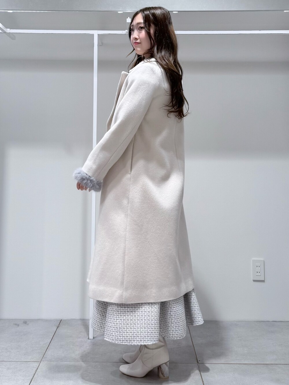 ホワイト系のチェスターコート、ホワイト系のスカート、グレー系のニット/セーターを着用したレディースの冬コーディネートの2枚目の写真