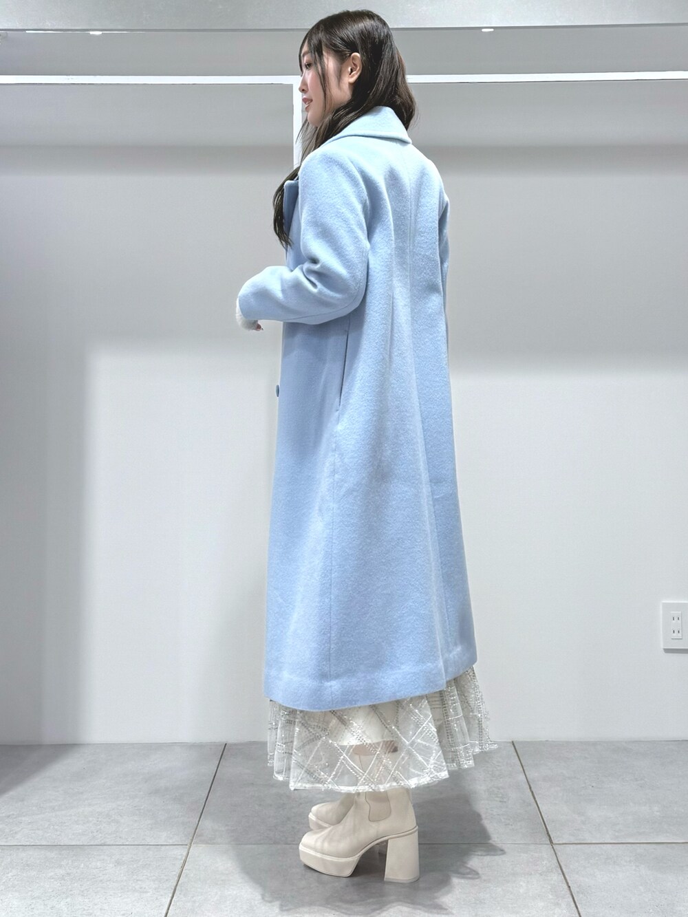 ブルー系のチェスターコート、ホワイト系のスカート、グレー系のカーディガン/ボレロを着用したレディースの秋コーディネートの3枚目の写真