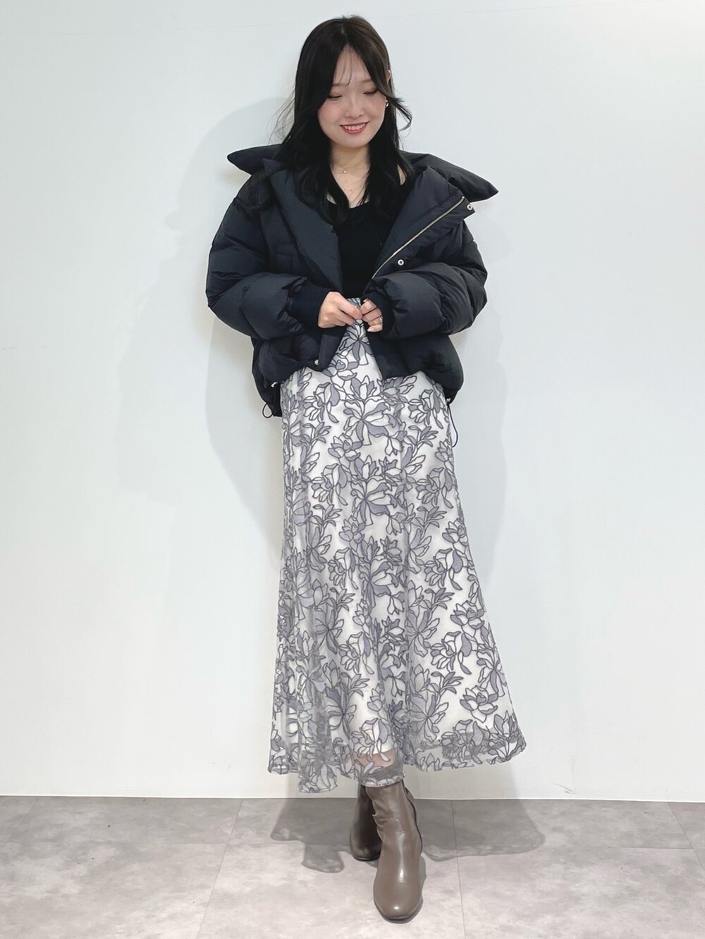 グレー系のスカート、ブラウン系のブーツ、ブラック系のダウンジャケット/コートを着用したレディースの冬コーディネートの2枚目の写真