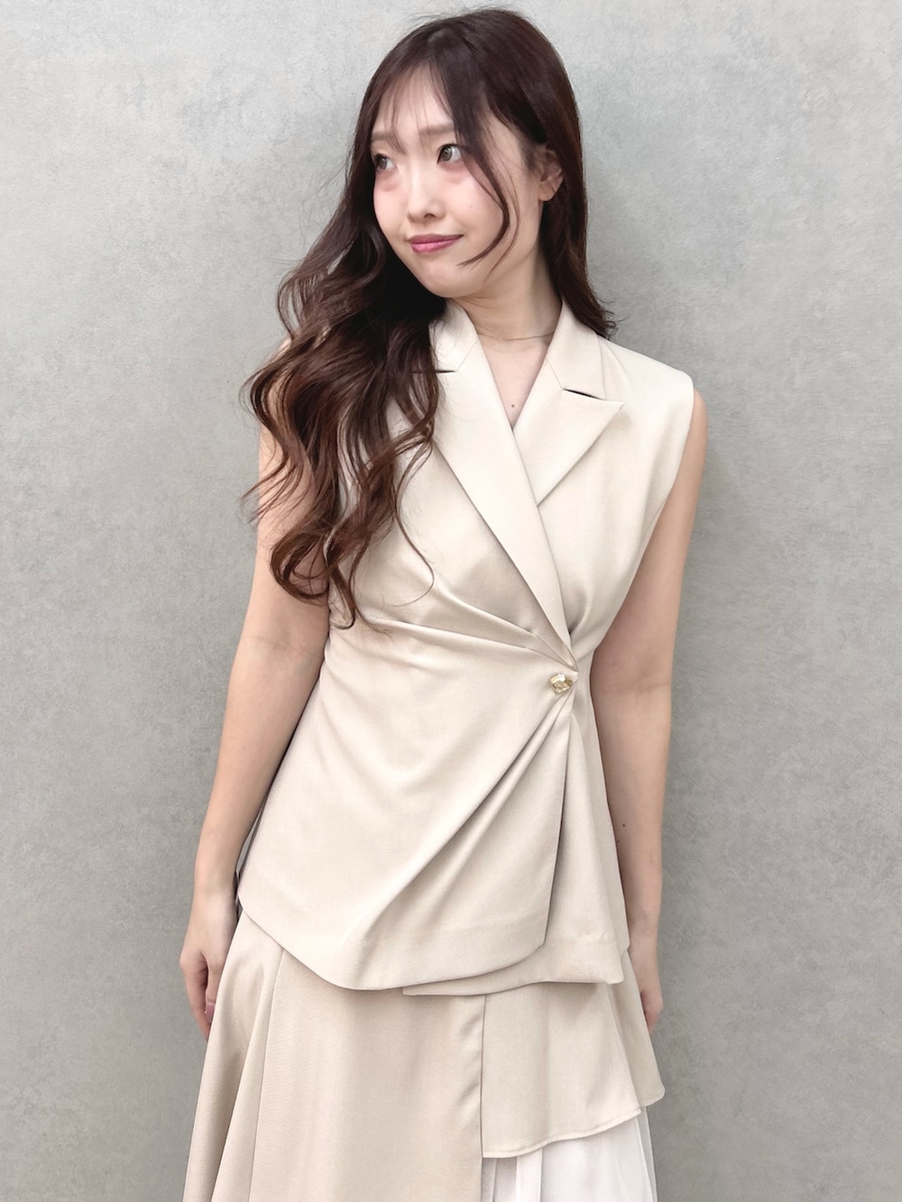 シルバー系のサンダル、ベージュ系のスカート、ベージュ系のベストを着用したレディースの春コーディネートの5枚目の写真